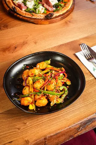 Crispy golden bites tossed with peppers, red onion and chilli, in a black bowl