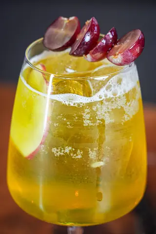 A golden sparkling drink with apple slices and red grapes