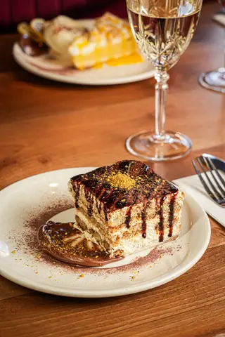 A slice of tiramisu with chocolate drizzle and chopped pistachio