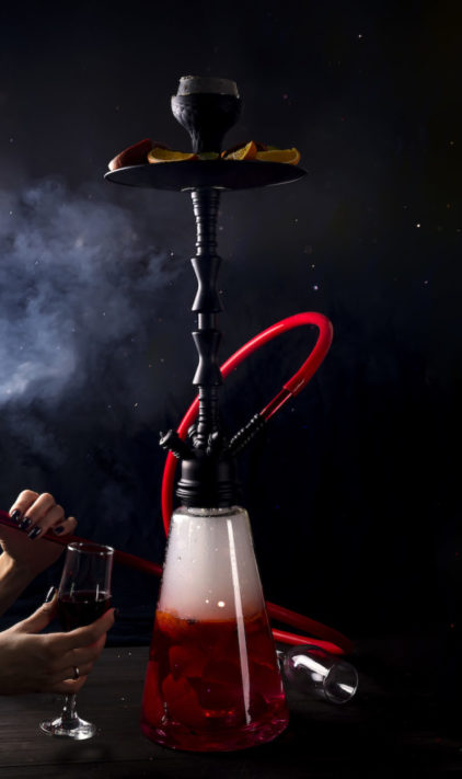A girl with a glass of red wine smokes a fruit hookah
